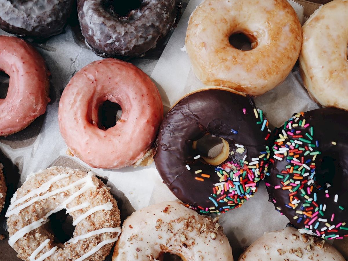 An assortment of donuts with various glazes and toppings, including sprinkles, chocolate, pink icing, and drizzle, neatly displayed together.