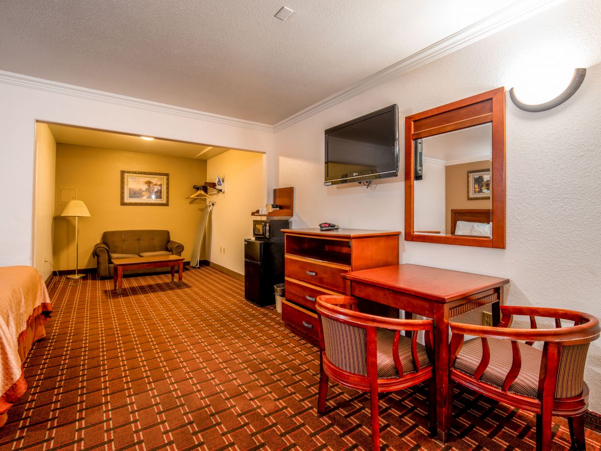 This image shows a hotel room with a bed, desk, chair, TV, and seating area with a lamp and sofa. The carpet has a geometric pattern.