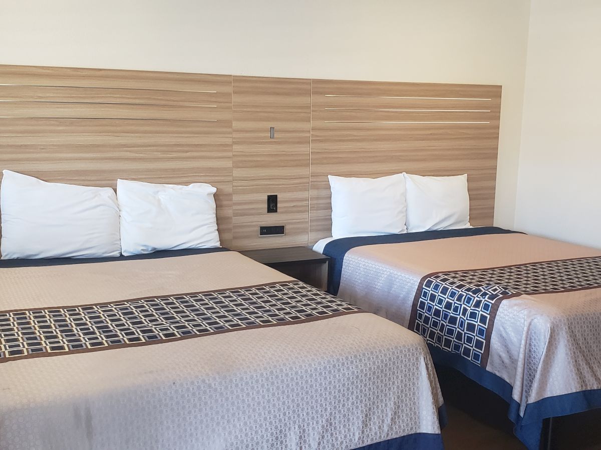 Two twin beds with white pillows and patterned blankets sit against a wooden headboard with decorative LED-style lines.