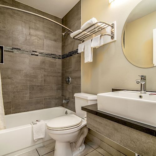 A modern bathroom with a bathtub, toilet, rectangular sink, mirror, and towel rack; neutral colors and clean design enhance its appeal.