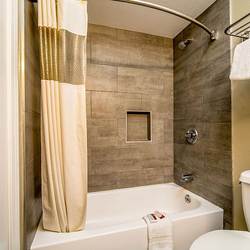 A modern bathroom featuring a bathtub with a shower curtain, toilet, and towels neatly arranged on a rack and the toilet tank.