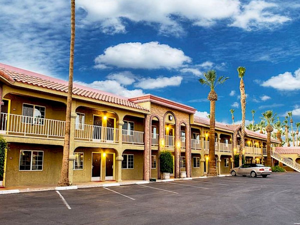 The image shows a two-story motel with parked cars, palm trees, and an expansive blue sky with clouds in the background.