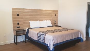 A neat bedroom with a double bed, white pillows, a blue-trim quilt, and matching wood headboard with side tables.