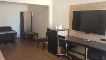 A modern hotel room with a desk, chair, flat-screen TV, small cabinet, and a door leading to another area.