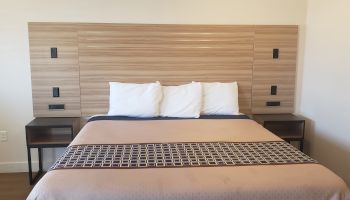 A neatly made bedroom with a bed, three pillows, patterned quilt, and matching wooden headboard/cabinet with side nightstands.