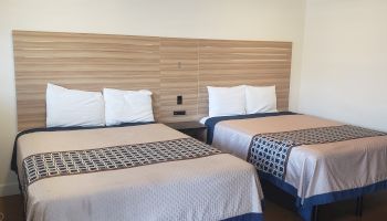 Two beds with white pillows and patterned blankets, facing a wood headboard with vertical cabinets in a tidy bedroom.