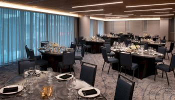 A banquet hall is set up with round tables, chairs, tableware, and floral centerpieces, ready for an event.