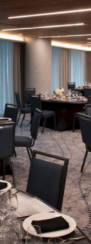 The image shows an elegantly set banquet hall with round tables, each adorned with black napkins, glasses, and candles, featuring modern decor and dim lighting.
