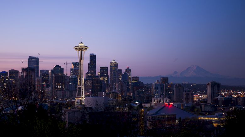 The image depicts a twilight view of the city skyline with the iconic Space Needle in Seattle, Washington, and Mount Rainier visible in the background.