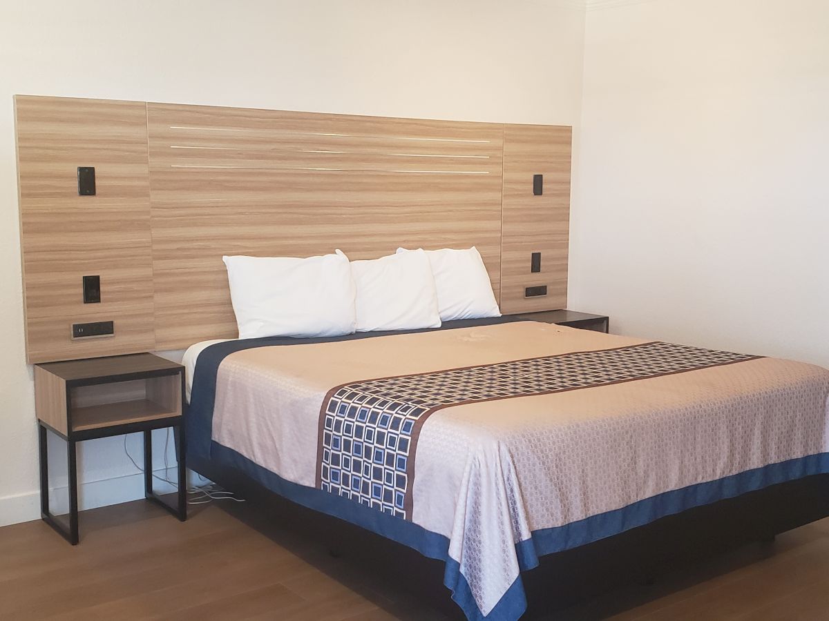 A tidy bedroom with a large bed, two pillows, and a wood headboard with built-in lights and outlets.
