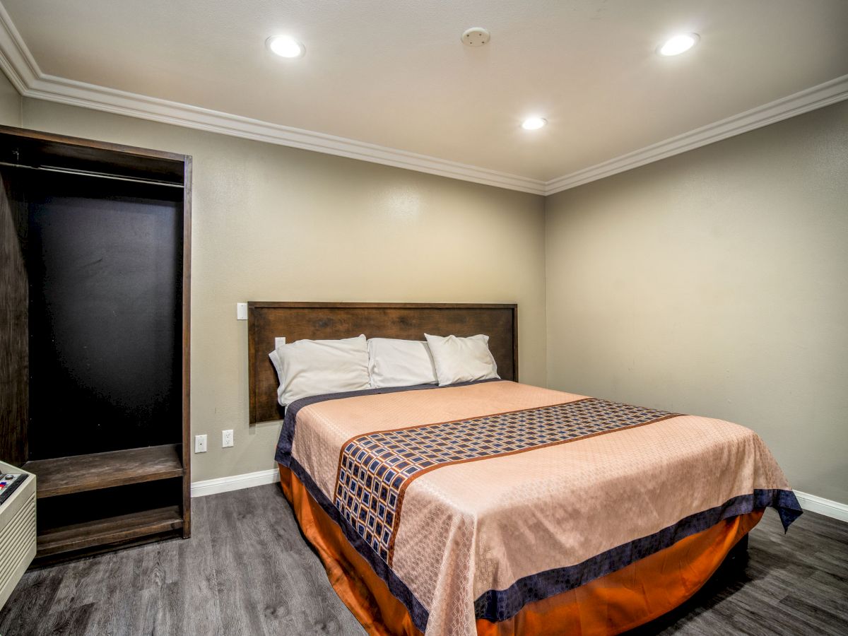 A minimalist bedroom with a large bed, simple bedding, wood flooring, an open wardrobe, and recessed lighting on the ceiling.